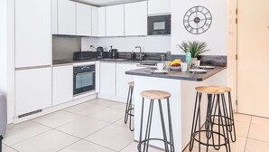 A modern kitchen with white cabinets, a black oven, a coffee maker, and a clock on the wall.