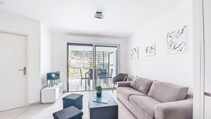 A modern living room with a sofa, two black ottomans, a coffee table, and a small side table. There is a sliding glass door leading to an outdoor area with a table and chairs.