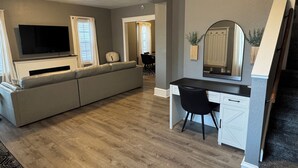 A modern living room with a grey sofa, a black desk, and a large flat-screen TV. - 4- Bedroom Retreat with Sauna, Game Room, Patio & Walk to Bars & Restaurants (Sheboygan)