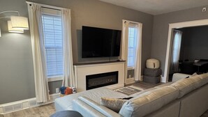 A modern living room with a large sofa, a fireplace, a flat-screen TV, and a dining area. - 4- Bedroom Retreat with Sauna, Game Room, Patio & Walk to Bars & Restaurants (Sheboygan)
