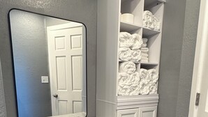 A bathroom with a white vanity, a large mirror, a black stool, and a white cabinet with towels. - 4- Bedroom Retreat with Sauna, Game Room, Patio & Walk to Bars & Restaurants (Sheboygan)