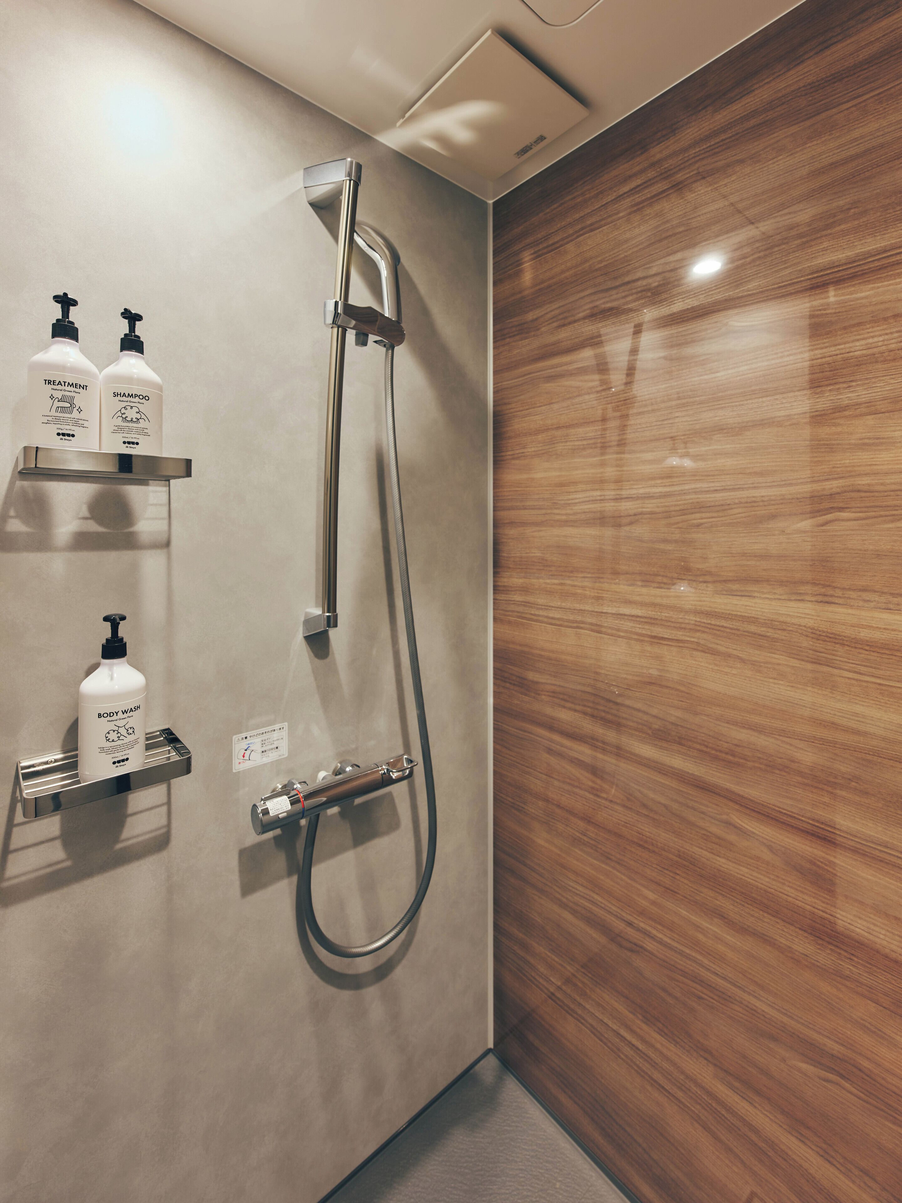 A shower area with a wall-mounted faucet and two bottles of shampoo and body wash on a shelf.