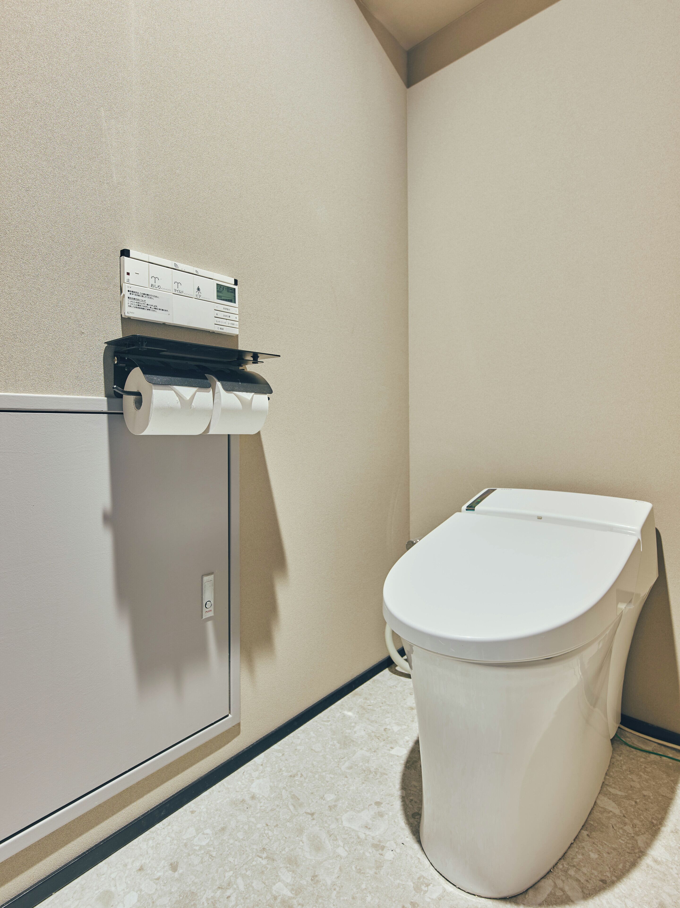 A bathroom with a toilet, a paper towel dispenser, and a wall-mounted control panel.