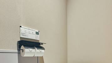 A bathroom with a toilet, a paper towel dispenser, and a wall-mounted control panel.
