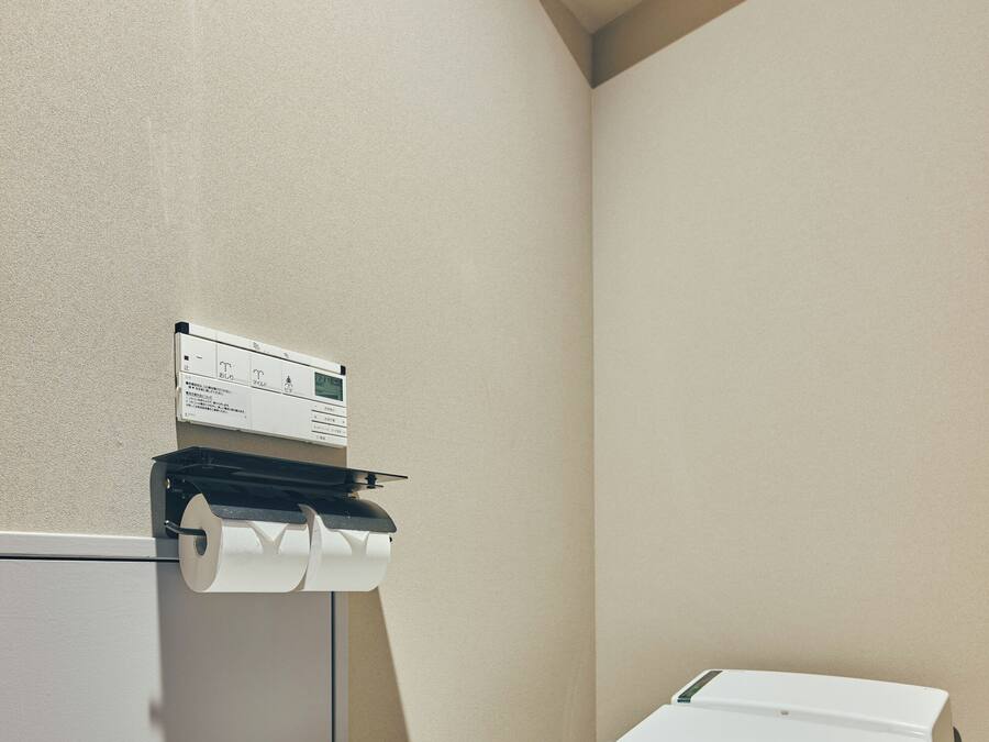 A bathroom with a toilet, a paper towel dispenser, and a wall-mounted control panel.
