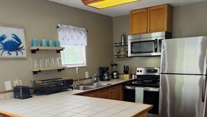 A kitchen with a central island, wooden stools, a microwave, a refrigerator, and a window with blinds. - Weeki Wachee Waterfront Canal home. Manatee Manor (Spring Hill)
