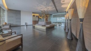 A spacious lobby with a modern design, featuring a seating area with sofas and chairs, a decorative plant, and a unique wall installation. - Apt with Reforma View - Pool and Jacuzzi (Mexico City)