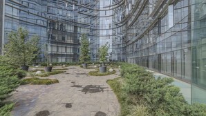 A modern building with a glass facade, a central courtyard with potted plants, and a patterned stone pathway. - Apt with Reforma View - Pool and Jacuzzi (Mexico City)