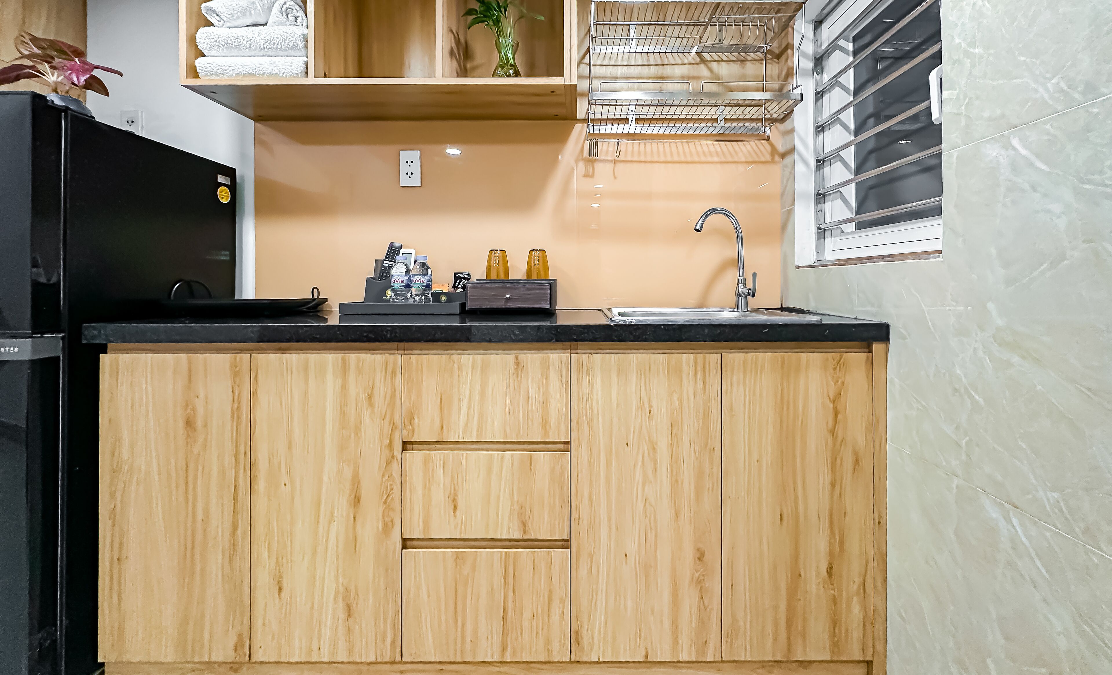 A kitchen with wooden cabinets, a black refrigerator, a sink, and a window with blinds.