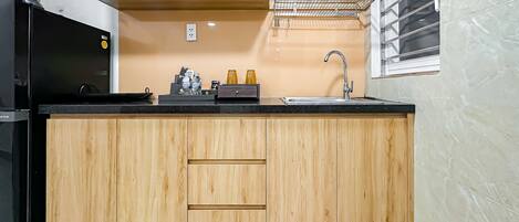 Una cocina con armarios de madera, un refrigerador negro, un lavamanos y una ventana con persianas.