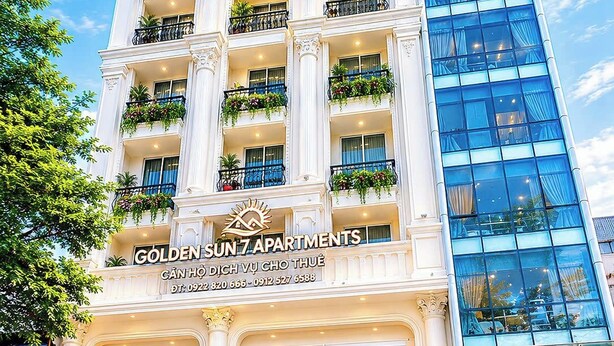 Un edificio de varios pisos con balcones, un cartel que dice 'GOLDEN SUN 7 APARTMENTS' y un moderno edificio de vidrio a la derecha.