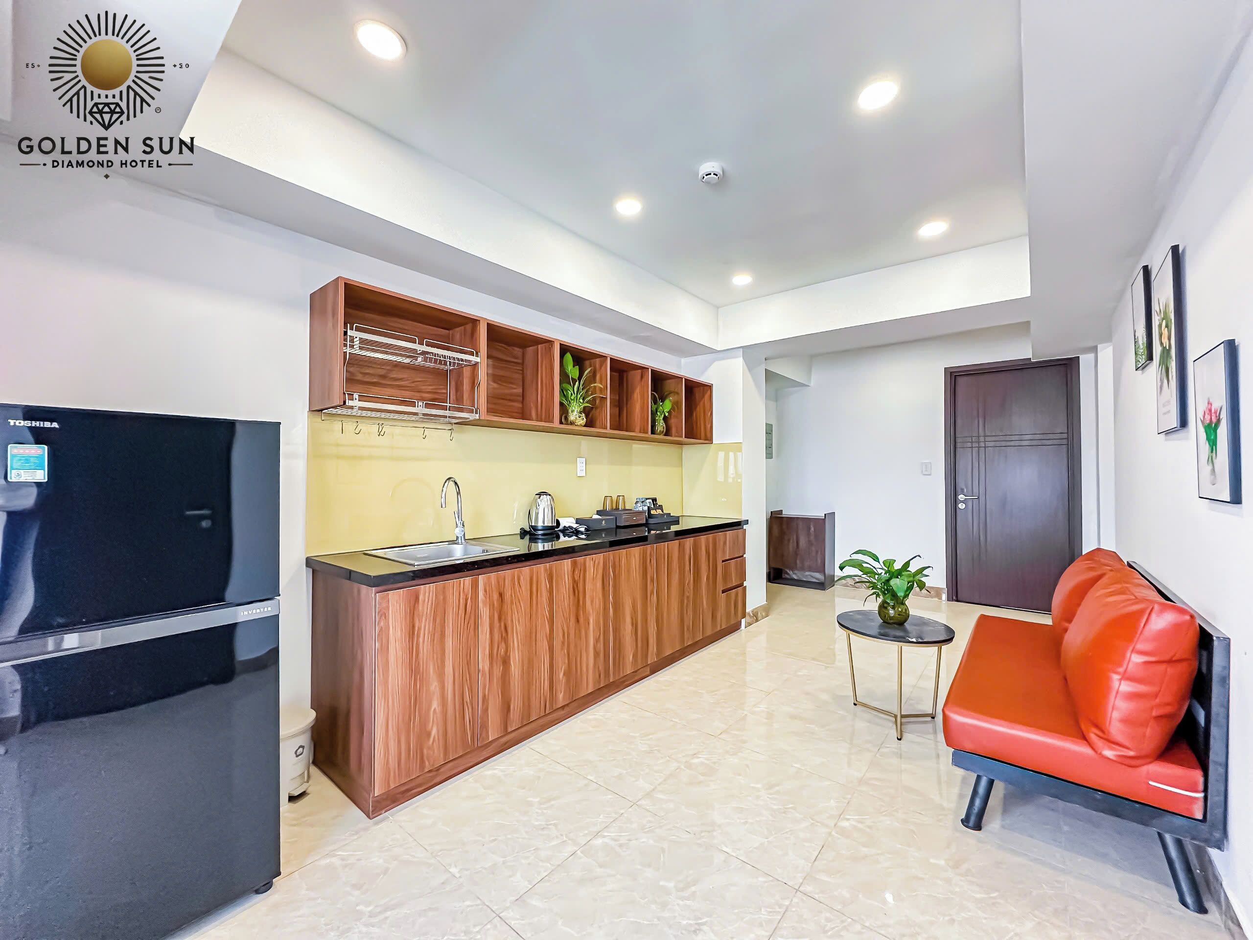 A modern kitchen with wooden cabinets, a black refrigerator, and a sink. There is a small dining area with a red chair and a table.