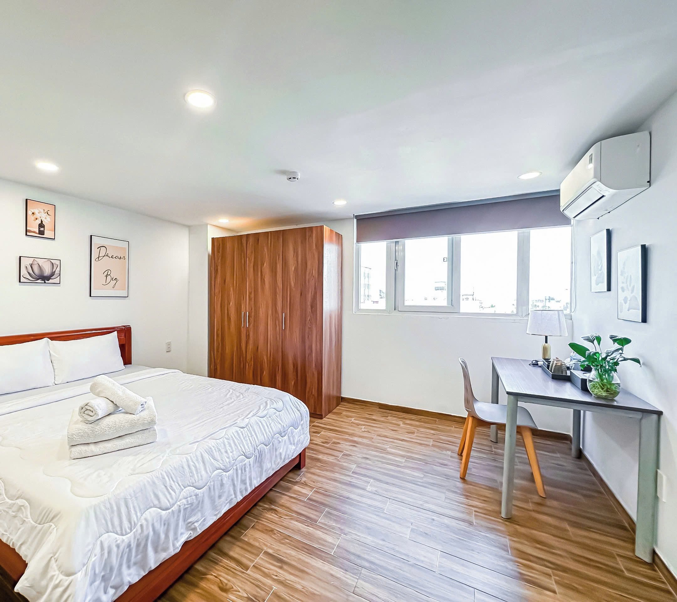 Een hotelkamer met een bed, een houten garderobe, een bureau met een stoel en een raam.