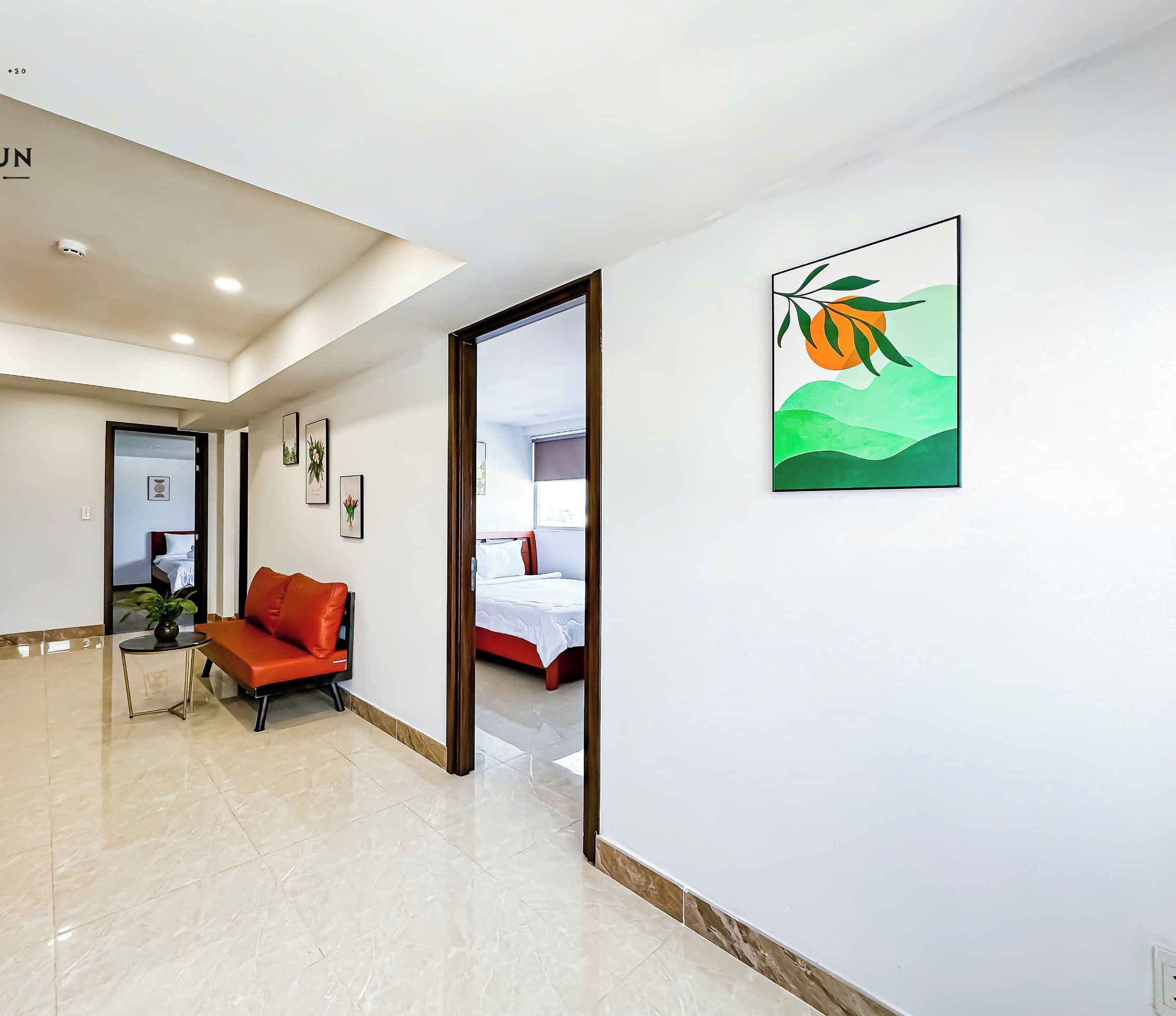 A hotel lobby with a reception desk, a seating area with a red sofa, framed artwork on the walls, and a bed visible through an open door.