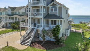 Une maison à plusieurs étages située en bord de mer, dotée d’un balcon, d’un escalier et offrant une vue sur l’océan.