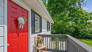 A red door with a white picket fence and a wooden chair with potted flowers on a porch. - Spotless Home Near Kings Island (Mason)