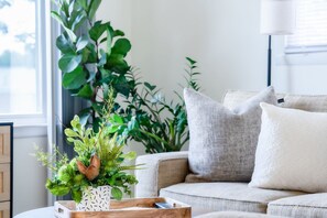 A living room with a beige sofa, a white cushion, and a wooden side table with a remote control. - Spotless Home Near Kings Island (Mason)
