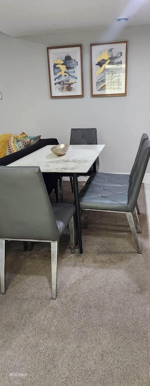 A dining area with a marble table, black upholstered chairs, and two abstract paintings on the wall. - The Vaulted Oasis (Airdrie)
