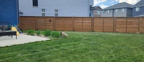 A backyard with a wooden fence, a patio with outdoor furniture, and a lawn.