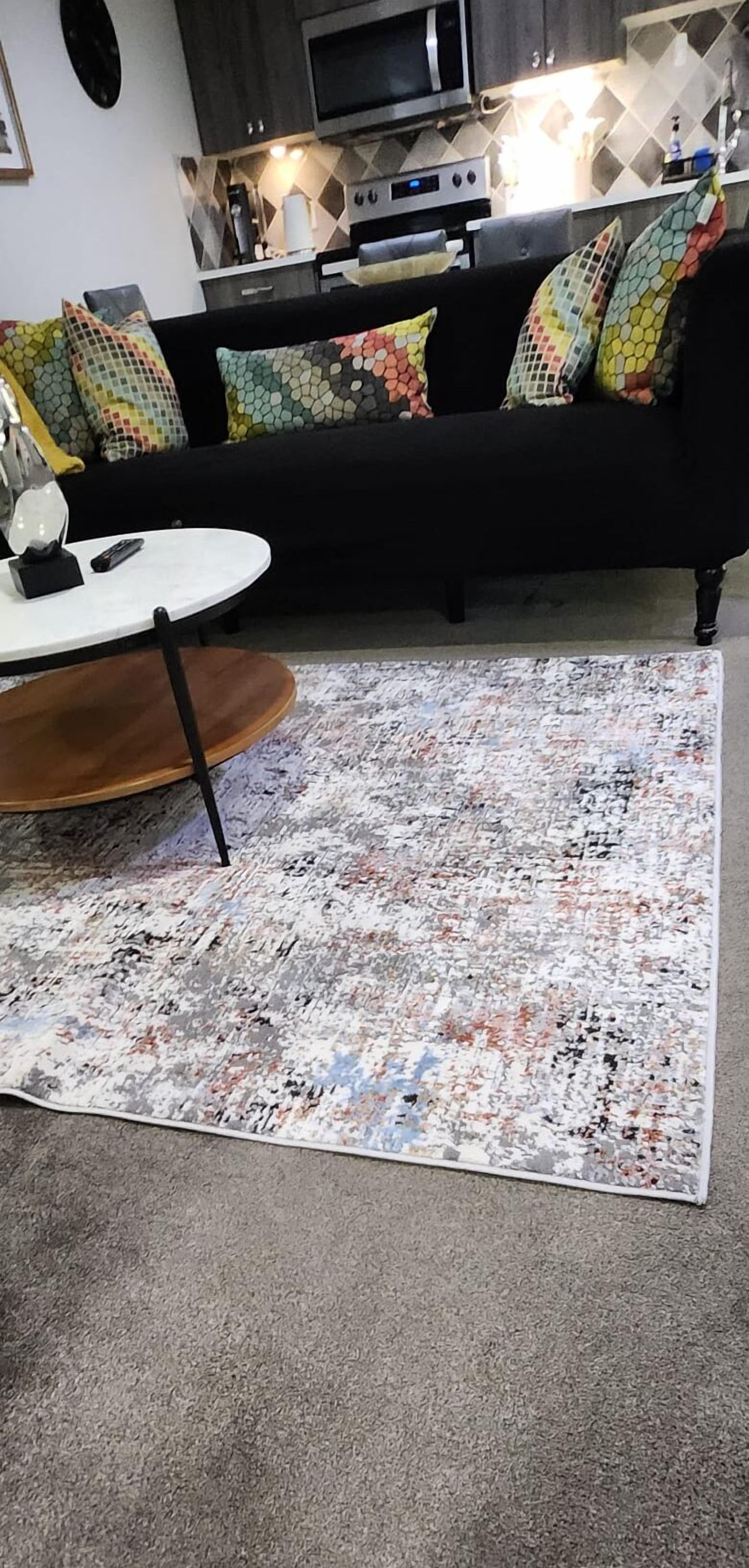 Ein Wohnzimmer mit einem schwarzen Sofa, bunten Kissen, einem weißen Couchtisch und einem gemusterten Teppich.