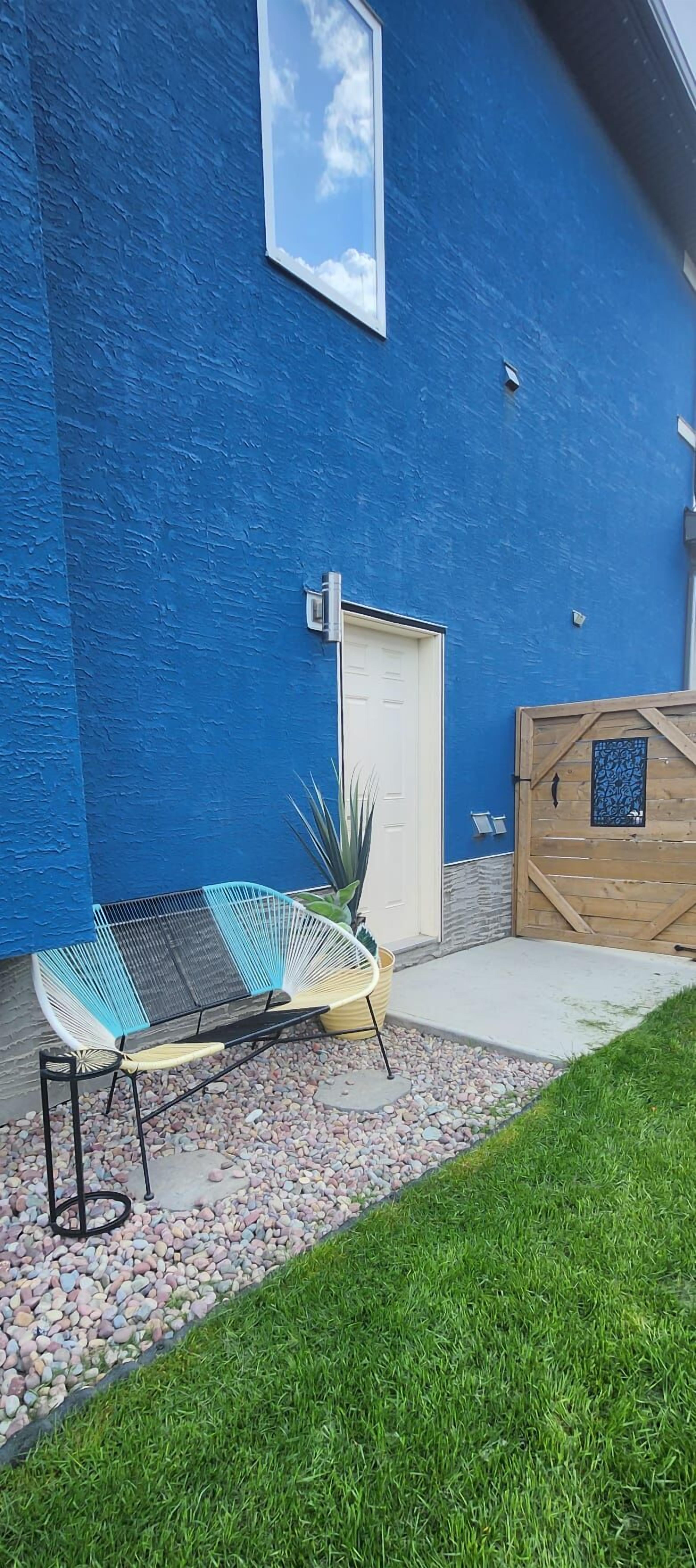 A blue house exterior with a white door, a wooden gate, and a bench with a metal frame.