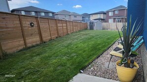 Un patio trasero residencial con cerco de madera, césped cuidado, un cobertizo pequeño y una planta en maceta.