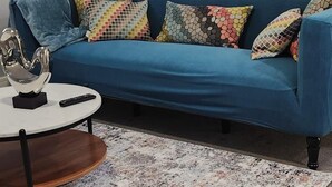 Una sala moderna con un sofá azul, cojines coloridos, una mesa de centro redonda y una alfombra estampada.