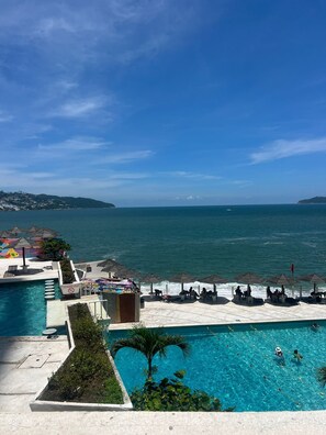 Ein Poolbereich mit klarem, blauem Wasser, Sonnenschirmen und Liegestühlen.