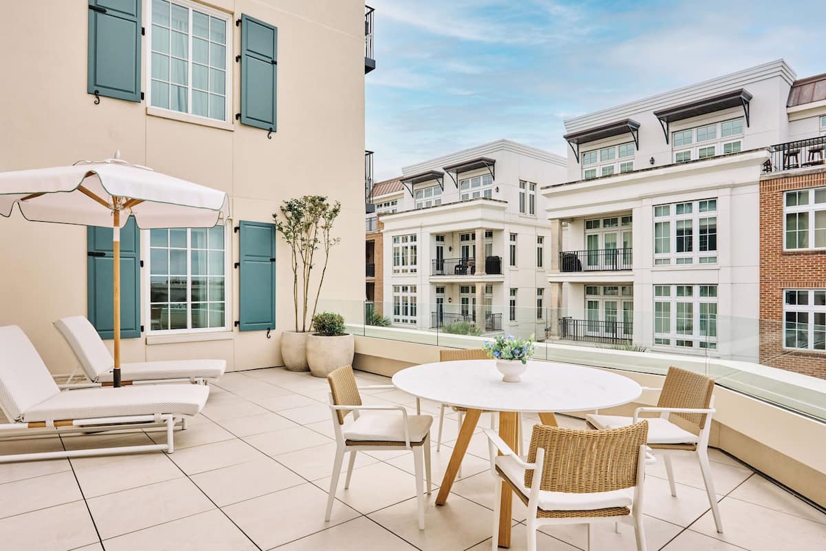 A balcony with a round table and chairs, a sun lounger, and a potted plant.