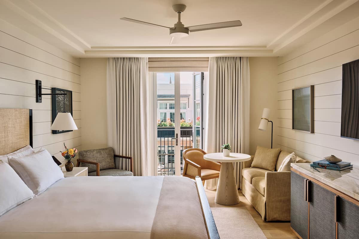 A hotel room with a bed, a desk, a chair, a round table, and a balcony with curtains.