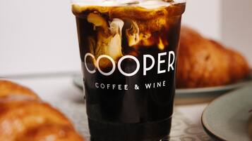 Una mano vertiendo leche en un vaso de café helado, con el texto 'COOPER COFFEE & WINE'.
