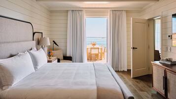 A bedroom with a bed, a nightstand, a lamp, a view of the ocean, and a door leading to a balcony.
