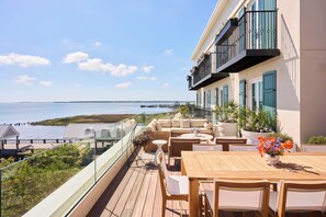 A balcony with a view of the sea, outdoor furniture, and potted plants. - The Cooper (Charleston)