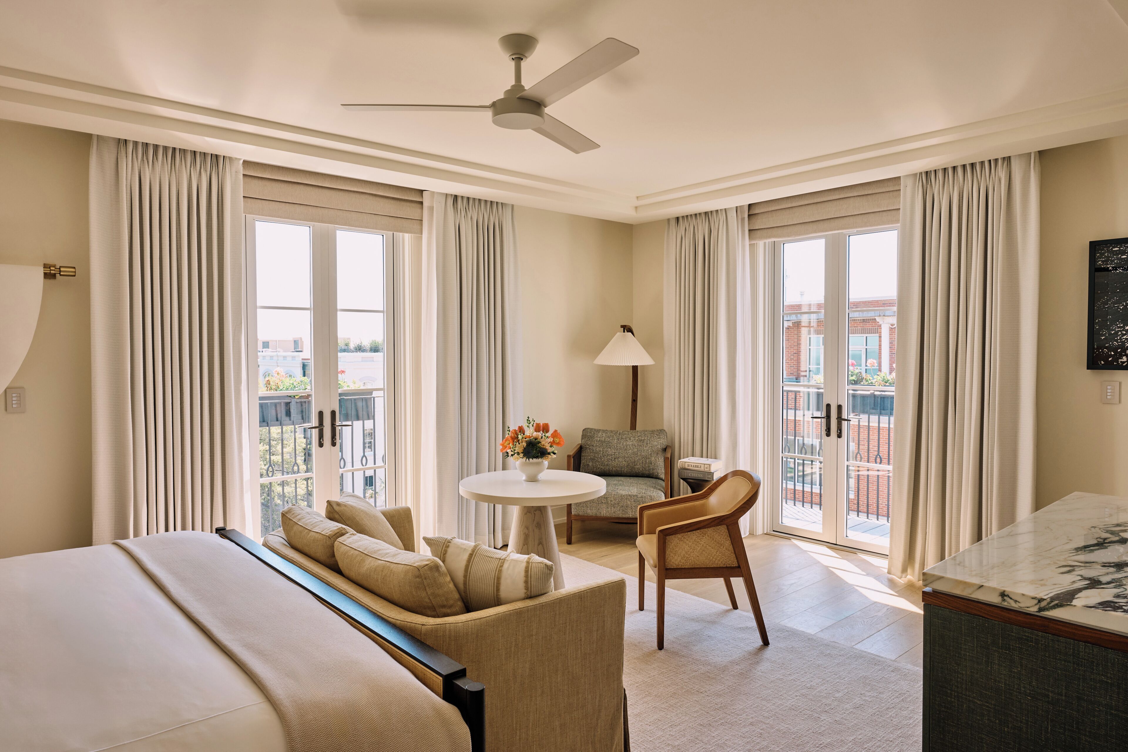 Una habitación de hotel con una cama, un sofá, una mesa de comedor, una silla, una lámpara y un ventilador de techo.
