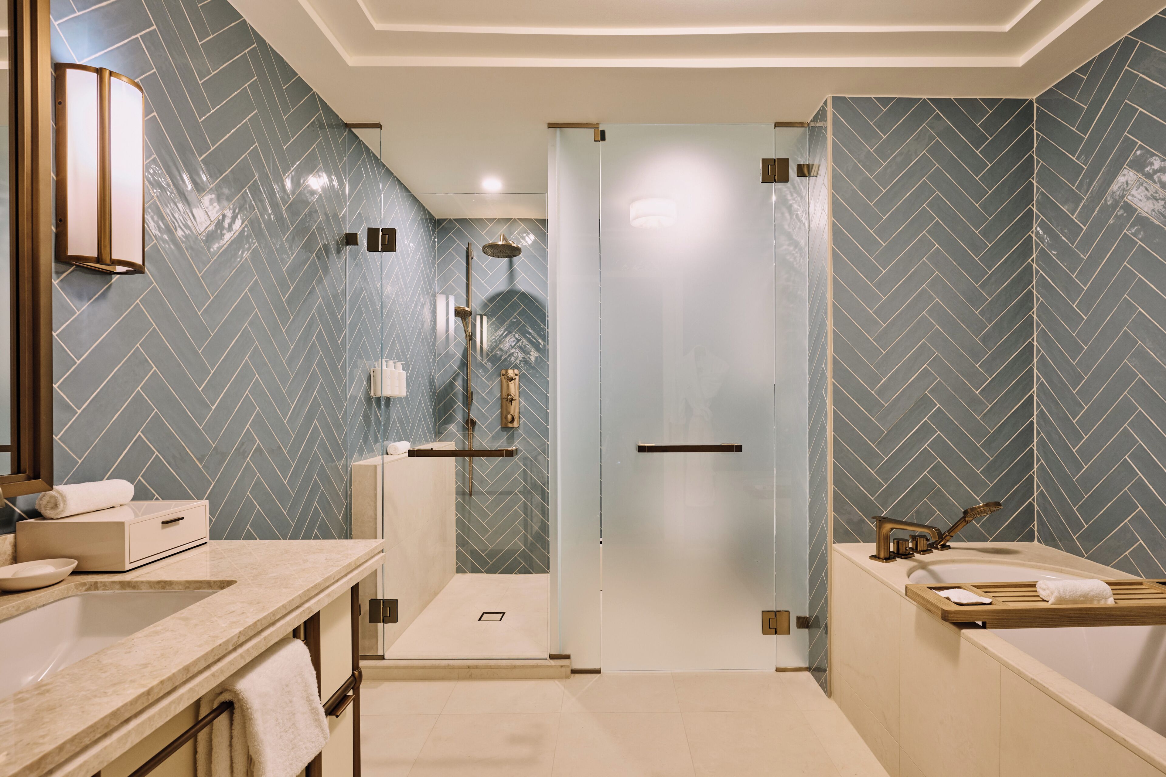A modern bathroom with a herringbone tile pattern, a glass shower enclosure, a vanity with a mirror, and a bathtub.