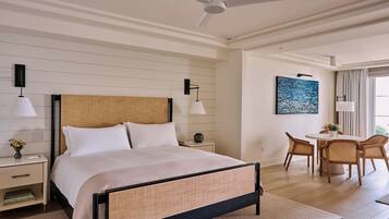 A hotel room with a bed, bedside tables, a desk, a chair, a ceiling fan, and a painting on the wall.