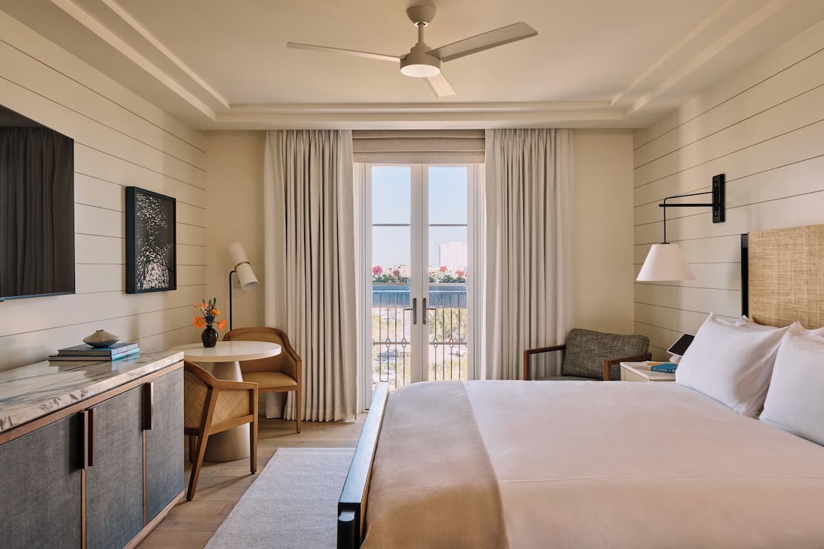 A hotel room with a bed, a desk, a chair, a window with curtains, and a ceiling fan.