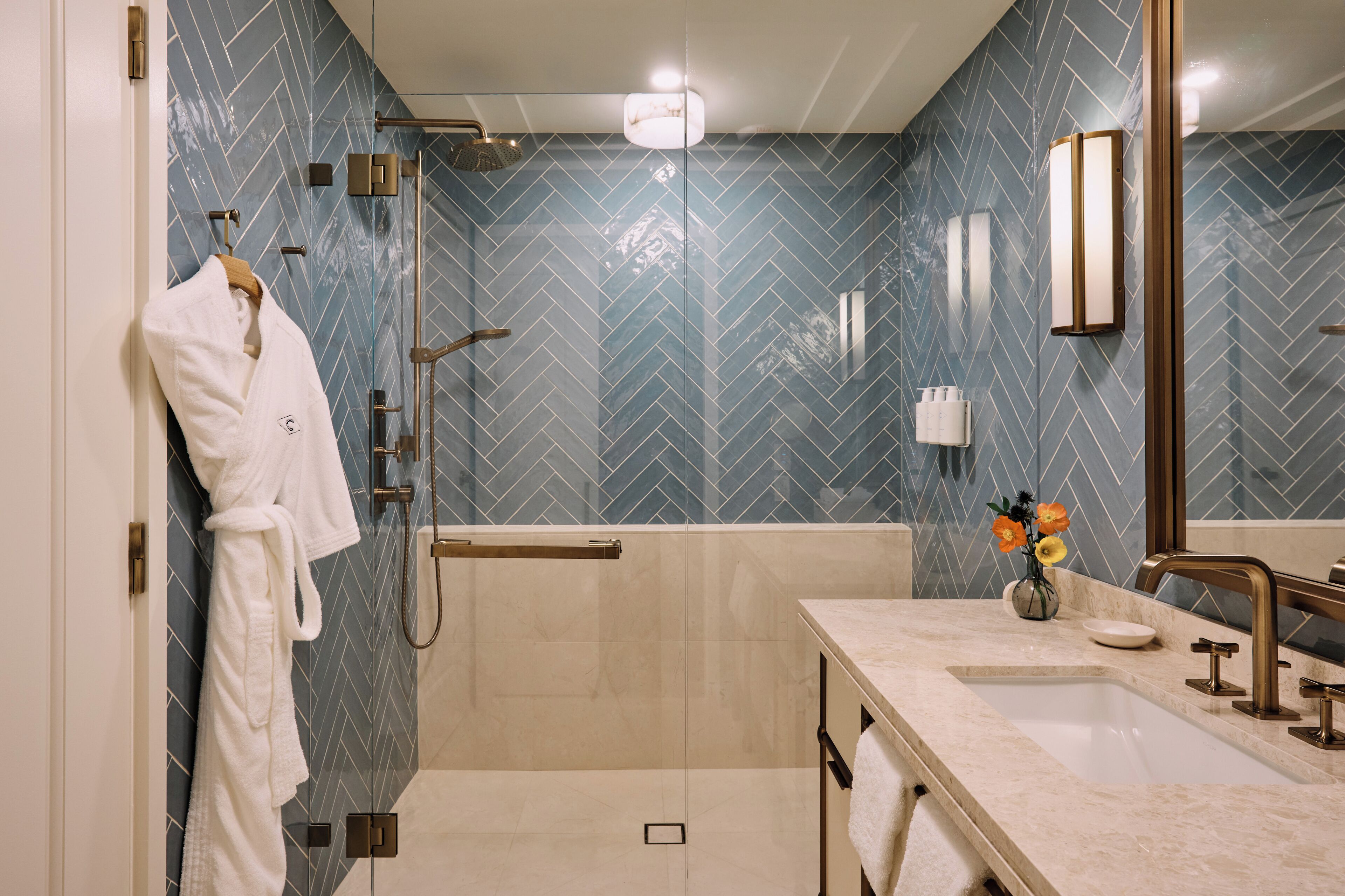 Une salle de bain moderne avec un carrelage disposé en motif chevron, une douche à l’italienne, un meuble-lavabo et un miroir.