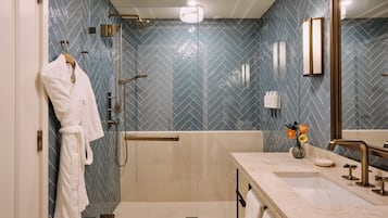 A modern bathroom with a herringbone tile pattern, a walk-in shower, a vanity with a sink, and a mirror.