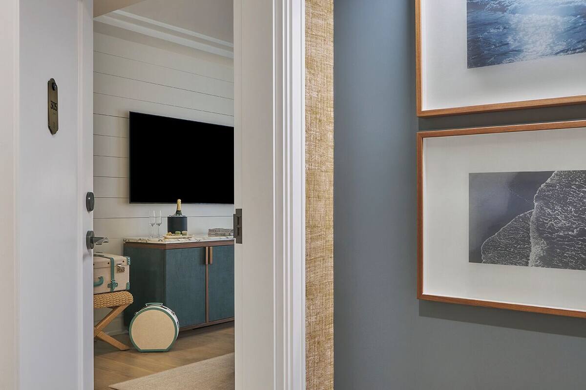 A hallway with a flat-screen TV mounted on the wall, a small table with a bottle and glasses, and a suitcase on the floor.
