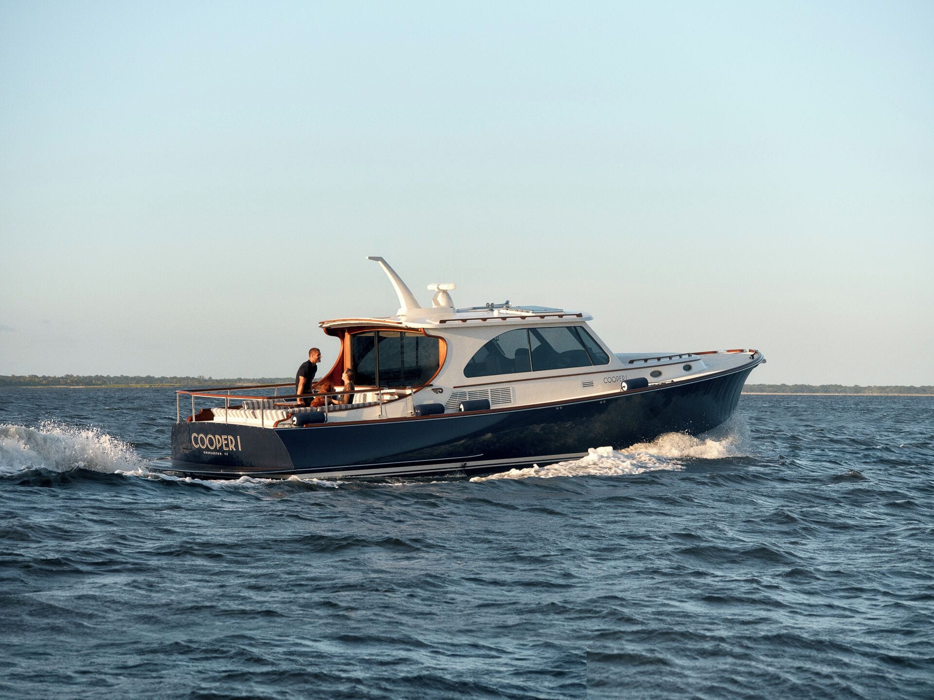 A boat named 'COOPER I' with a cabin and a helipad on top, moving through a body of water.