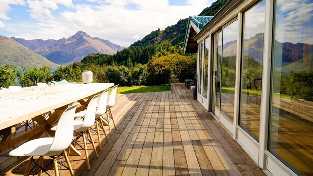 Een houten terras met een tafel en stoelen, met uitzicht op een bergachtig landschap.