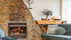 Een stenen openhaard met vuur, een grijze bank en een houten plank met decoratieve objecten.