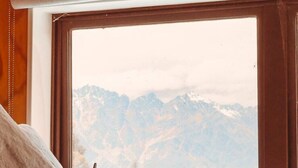 Ein Zimmer mit Holzboden, einem Fenster mit Bergblick und einem Bett mit Kissen.
