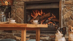 Ein gemütlicher Raum mit Kamin aus Stein, einem Holztisch und zwei Hunden.