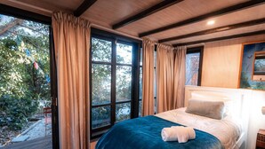 A bedroom with a large window, a bed with a blue blanket, and a headboard.