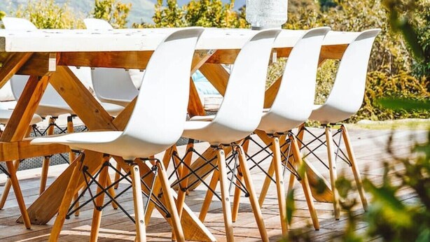 A dining table with white chairs and a glass pitcher, set outdoors with a mountain view in the background.