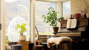 A cozy room with a piano, a guitar, a drum, and a large window with a view of mountains.