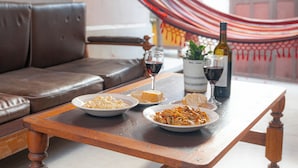 Uma mesa de jantar com pratos de comida, copos de vinho e uma garrafa de vinho. Uma rede e um vaso de planta estão ao fundo.