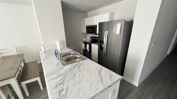 A modern kitchen with a marble countertop, stainless steel appliances, and a dining area with a wooden table and white chairs. - Home featuring 3 Rooms 1 Bath Sleeps 6 Guest (Roxboro)